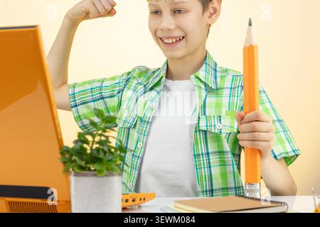 Happy Schoolboy Holding Pencil And Flexing Arm At Desk With Laptop Stock Photo