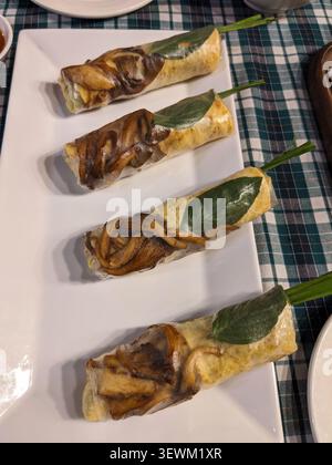Four fresh Vietnamese spring rolls filled with mushrooms and herbs are presented on a white plate, ready to be enjoyed Stock Photo