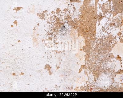 White plaster peeling from an old concrete wall creating a textured background Stock Photo