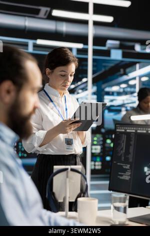 Data center engineer uses a digital tablet in a data center to manage AI virtualization and optimize server infrastructure. Stock Photo