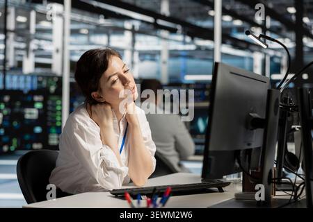 Exhausted system administrator handles fatigue in a data center after a long hardware troubleshooting session at a computer workstation. Stock Photo