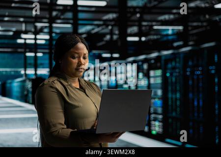 System operator uses a laptop computer in a data center to monitor equipment, manage workflows, and support reliable infrastructure. Stock Photo