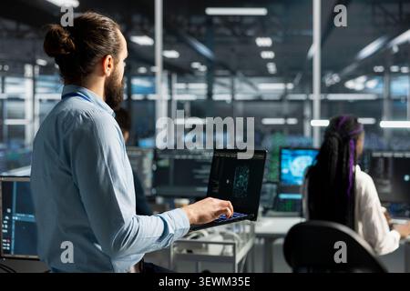 Data center engineer uses a laptop to manage AI training datasets and database workflows inside a server room. Stock Photo
