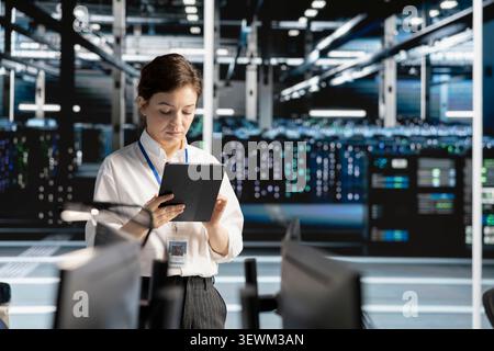 Data center engineer reviews AI systems and neural network parameters on a tablet inside a data center. Stock Photo