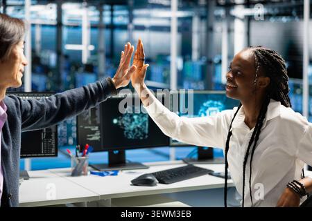 Delighted data center colleagues share a high five after improving system efficiency and completing AI implementation. Stock Photo