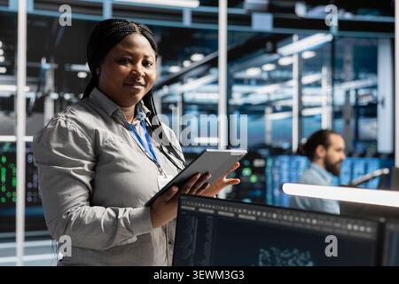 Smiling data center programmer uses a tablet to review server infrastructure, diagnostics and AI technology in a data center. Stock Photo