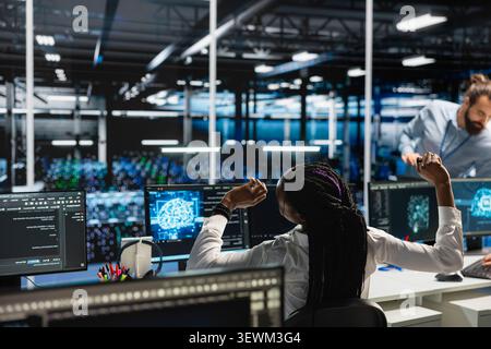 African American woman stretches at a workstation in a server farm to relieve back fatigue after long technical work. Stock Photo