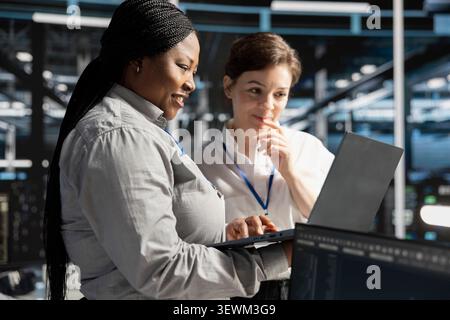 Smiling data center team works with digital devices while reviewing systems, scripts and server infrastructure. Stock Photo