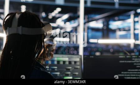 Administrator wears a headset in a server farm, using artificial intelligence troubleshooting to assist users. Stock Photo