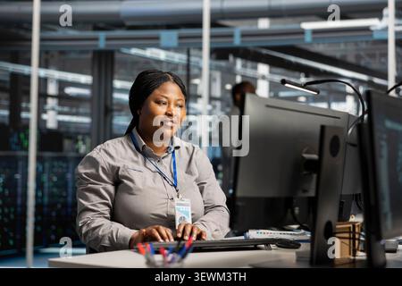 Smiling system administrator uses a computer to review server infrastructure, diagnostics and AI technology in a data center. Stock Photo