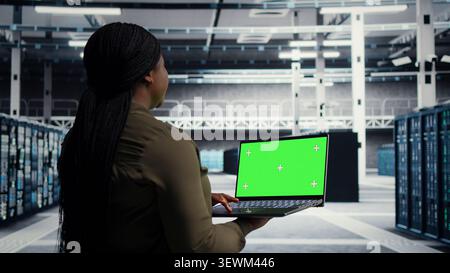 Data center engineer uses green screen laptop in a data center to inspect hardware and maintain system stability. Stock Photo