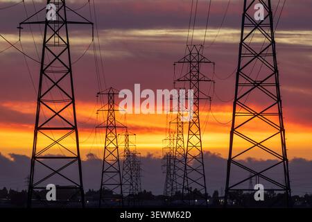 A corridor of high-voltage electrical transmission towers silhouetted against a brilliant sunset sky. Palo Alto Baylands. Stock Photo