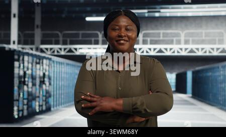 Smiling data center administrator walks through a server room while reviewing security compliance and cyber risk. Stock Photo
