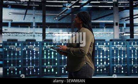 Programmer uses tablet in a server farm to plan disaster recovery and strengthen data protection. Stock Photo
