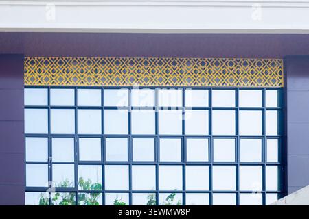 Modern glass grid reflects soft blue sky. Golden patterned border adds architectural contrast. Green leaves peek through lower frame. Clean lines suggest urban elegance or contemporary design Stock Photo