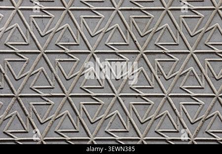 Geometric carved stone wall pattern featuring interconnected triangular and abstract interlocking shapes in grey concrete Stock Photo