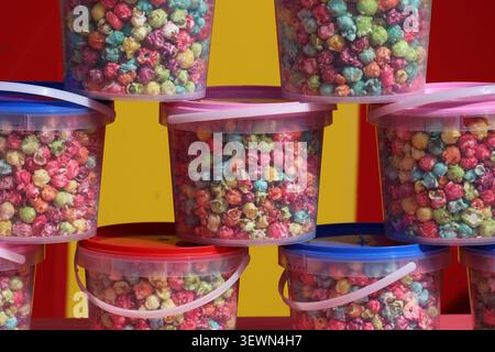 Brightly coloured rainbow popcorn packed in clear plastic buckets with handles stacked on display at a carnival or market Stock Photo