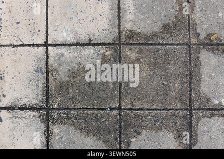 Overhead full frame texture of damp and weathered square concrete pavers with dark dirt in the grout lines Stock Photo