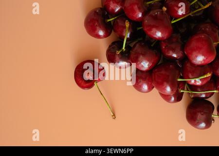 Fresh red cherries with stems on a peach background, top view with copy space and a few scattered fruits Stock Photo