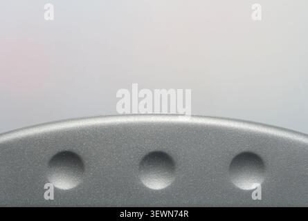 Minimalist macro shot of a curved grey plastic surface featuring three evenly spaced circular dimples against a pale background Stock Photo