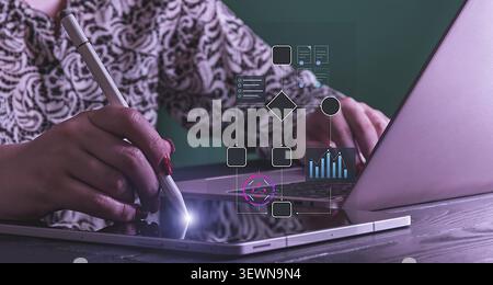A businesswoman's hands are seen multitasking, using a digital stylus on a tablet while working on a laptop Stock Photo