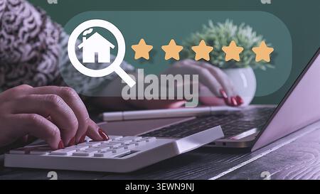 A businesswoman's hands are seen using a calculator and laptop, overlaid with a futuristic graphic of a house inside a magnifying glass next to a five Stock Photo