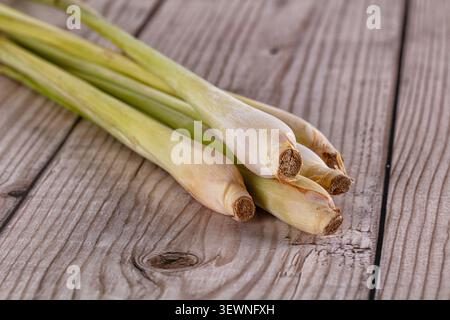 Fresh lemongrass stalks arranged diagonally on weathered wood surface. Natural lighting highlights pale green cream tones. Rustic composition with sha Stock Photo