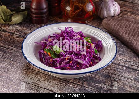 Vibrant purple shredded cabbage salad in white enamel bowl with blue rim. Garnished with green herbs orange specks. Set on weathered wood surface with Stock Photo