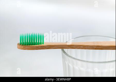 Eco-friendly bamboo toothbrush with green bristles balanced on a clear glass, photographed in close-up against a clean white background in an oral car Stock Photo