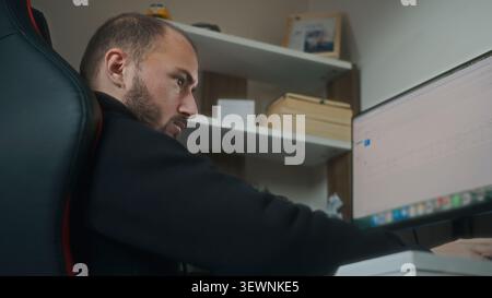 A concentrated man is working intently on a computer in a home office environment. Stock Photo