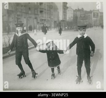 Berlin, roller skating, children, girls, boys, leisure, fun, middle class, Three children on roller skates holding hands and skating in the street, Ph Stock Photo