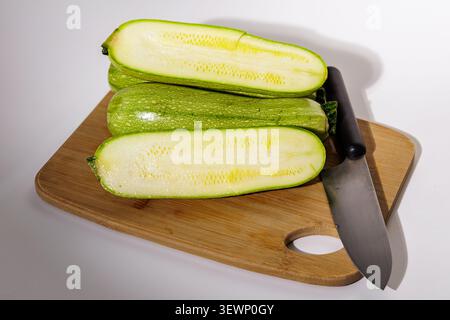 Green zucchini, sliced. The internal structure with seeds is visible. The zucchini lies on a wooden board. White background, close-up. Stock Photo