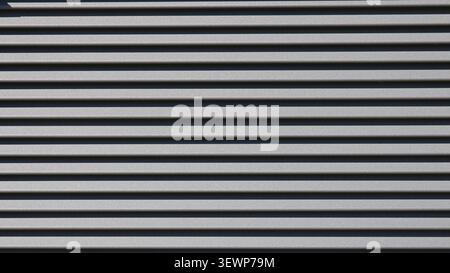 Gray metal siding texture with crisp horizontal lines. Corrugated matte panels create a three-dimensional geometric pattern with chiaroscuro. Stock Photo