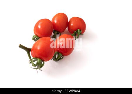 Five cherry tomatoes are placed together on a white surface. They are small, round, and have a shiny skin. The stems show green leaves connecting them Stock Photo