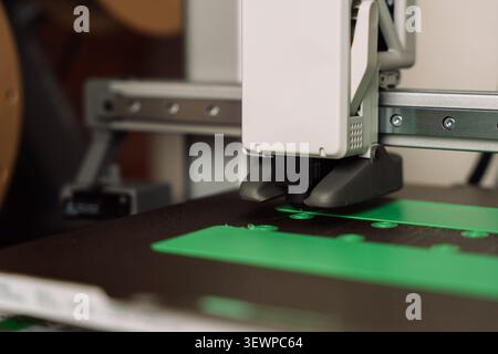 Desktop 3D printer creating green plastic parts on build plate in close-up view Stock Photo