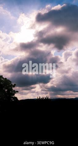 Sun rays breaking through dramatic storm clouds above a silhouetted landscape. Stock Photo