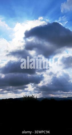 Bright sun rays breaking through dark storm clouds in the daytime sky. Stock Photo
