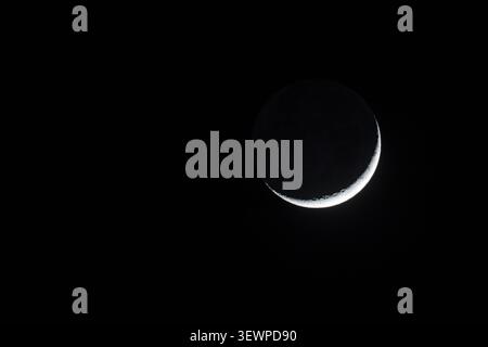 Waxing crescent moon shining brightly against a completely pitch black night sky in California, minimalist astrophotography. Stock Photo