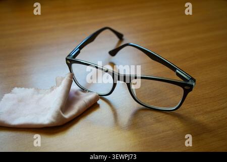 A pair of modern, black-rimmed reading glasses resting on a smooth wooden tabletop. Stock Photo