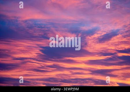 Sunset paints drifting clouds in glowing shades of pink purple and gold across the evening sky Stock Photo