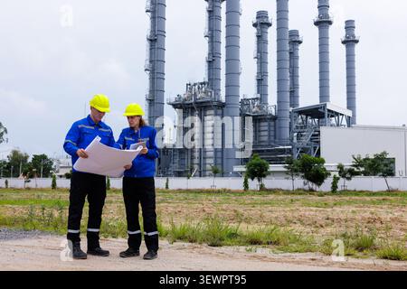 Two engineers in safety helmets and uniforms discuss project plans at a power generating facility. Stock Photo