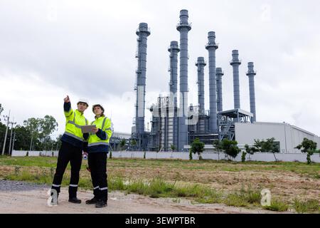 Professional industrial engineers in high visibility safety vests and hard hats analyze plant site plans using a tablet computer outdoors. Stock Photo