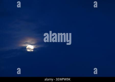 full moon floating and covering by dark cloud on blue sky in twilight background Stock Photo