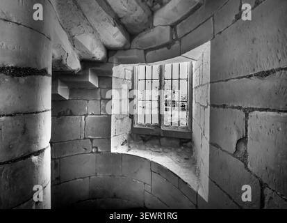 Moody light spills through a leaded window above a spiral staircase inside Old Wardour Castle in Wiltshire UK creating a fine-art monochrome image Stock Photo