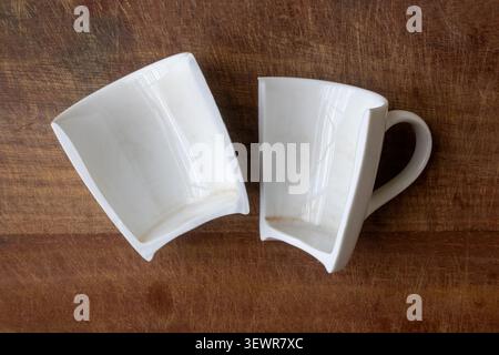 Two shards of a shattered porcelain coffee mug with handle placed on a brown wood background. Perfect commercial imagery for household accidents, emot Stock Photo