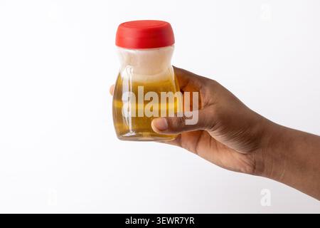 Close-up of a hand holding a small transparent jar filled with pure golden honey with a red plastic cap on white. Ideal for organic sweet food marketi Stock Photo