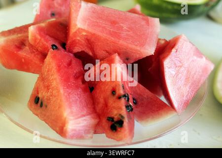 Watermelon slices are arranged on a clear glass plate, showing vibrant red flesh with black seeds, providing a refreshing and juicy fruit snack perfec Stock Photo