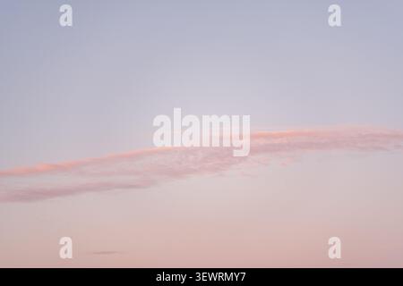 Minimal pastel evening sky with a delicate pink cloud illuminated by the setting sun. The image creates a calm and peaceful atmosphere with abundant c Stock Photo