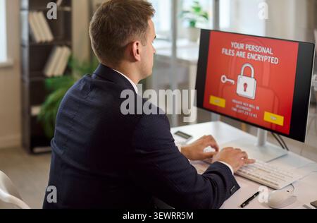 Businessman facing ransomware alert on office computer, data security breach risk Stock Photo
