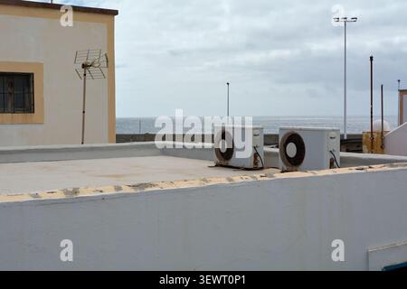 Coastal building rooftop with external AC units facing the sea, representing summer cooling, climate control, energy consumption, and seaside real est Stock Photo